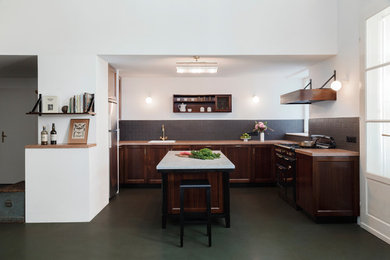Offene Klassische Küche mit Landhausspüle, dunklen Holzschränken, Arbeitsplatte aus Terrazzo, Küchenrückwand in Schwarz, Rückwand aus Metrofliesen, schwarzen Elektrogeräten, Betonboden, Kücheninsel, grauem Boden und Schrankfronten im Shaker-Stil in Sonstige