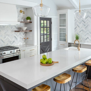 Idée de décoration pour une grand cuisine américaine tradition en U avec un évier encastré, un placard à porte shaker, des portes de placard blanches, un plan de travail en quartz, une crédence grise, une crédence en marbre, un électroménager en acier inoxydable, un sol en bois foncé, un îlot central, un sol marron et un plan de travail blanc.