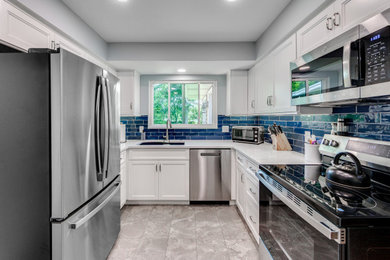 Example of a small transitional u-shaped vinyl floor and gray floor kitchen design in St Louis with a double-bowl sink, shaker cabinets, white cabinets, quartz countertops, blue backsplash, subway tile backsplash, stainless steel appliances and white countertops