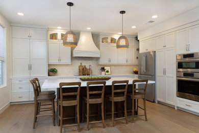 Mid-sized l-shaped medium tone wood floor and brown floor open concept kitchen photo in San Diego with a farmhouse sink, shaker cabinets, white cabinets, quartz countertops, white backsplash, ceramic backsplash, stainless steel appliances, an island and white countertops