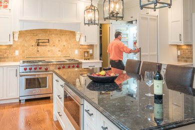 This is an example of a large traditional u-shaped eat-in kitchen in Boston with a farmhouse sink, beaded inset cabinets, white cabinets, granite benchtops, medium hardwood floors, with island and brown floor.