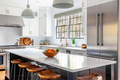 Mid-sized beach style l-shaped medium tone wood floor kitchen photo in Chicago with an undermount sink, shaker cabinets, white cabinets, quartz countertops, white backsplash, stainless steel appliances, an island, white countertops and subway tile backsplash