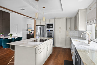Inspiration for a mid-sized transitional l-shaped medium tone wood floor, brown floor and tray ceiling eat-in kitchen remodel in Dallas with a farmhouse sink, shaker cabinets, brown cabinets, marble countertops, white backsplash, mosaic tile backsplash, stainless steel appliances, an island and white countertops