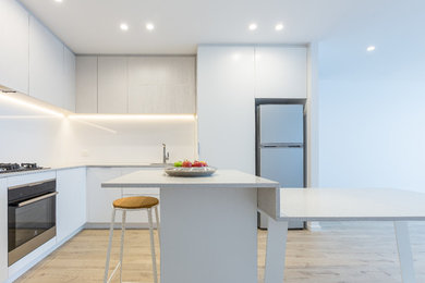 Design ideas for a mid-sized modern l-shaped open plan kitchen in Melbourne with an undermount sink, open cabinets, white cabinets, quartz benchtops, white splashback, glass sheet splashback, black appliances, laminate floors, with island, beige floor and grey benchtop.