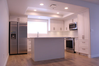 Exempel på ett mellanstort modernt kök, med en undermonterad diskho, skåp i shakerstil, vita skåp, bänkskiva i kvarts, vitt stänkskydd, stänkskydd i sten, rostfria vitvaror, ljust trägolv, en köksö och beiget golv