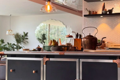Photo of an expansive contemporary u-shaped home bar in Hertfordshire with a submerged sink, floating shelves, black cabinets, stainless steel worktops, white splashback, porcelain flooring, grey floors, white worktops and feature lighting.