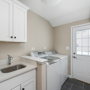 Ejemplo de cuarto de lavado lineal, clásico, pequeño, con fregadero bajoencimera, armarios estilo shaker, puertas de armario amarillas, encimera de acrílico, paredes beige, suelo de pizarra, lavadora y secadora juntas, suelo negro y encimeras beige