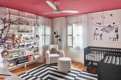 Imagen de habitación de bebé niña moderna pequeña con paredes blancas y suelo de madera en tonos medios