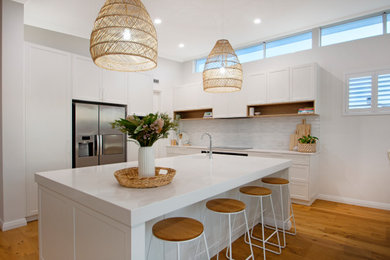 Photo of a large contemporary l-shaped eat-in kitchen in Perth with a drop-in sink, flat-panel cabinets, white cabinets, quartz benchtops, white splashback, ceramic splashback, stainless steel appliances, medium hardwood floors, with island, brown floor and white benchtop.