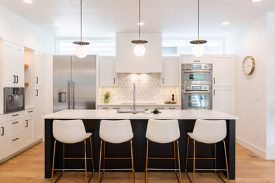 Example of a transitional l-shaped medium tone wood floor and brown floor open concept kitchen design in Boise with an undermount sink, shaker cabinets, white cabinets, quartz countertops, white backsplash, porcelain backsplash, stainless steel appliances, an island and white countertops