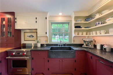 Inspiration for a traditional kitchen in Bridgeport with a farmhouse sink, shaker cabinets, red cabinets, soapstone benchtops, black splashback, stainless steel appliances, medium hardwood floors, no island and black benchtop.