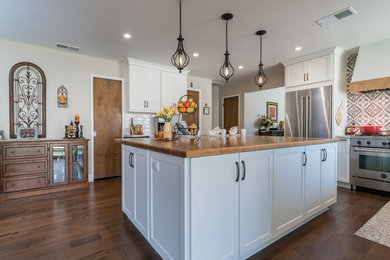Example of a large country l-shaped dark wood floor and brown floor open concept kitchen design in Other with a farmhouse sink, shaker cabinets, white cabinets, granite countertops, white backsplash, subway tile backsplash, stainless steel appliances, an island and gray countertops