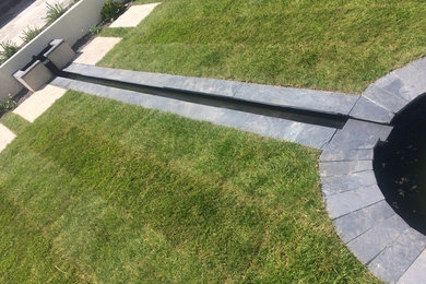 This is an example of a mid-sized contemporary backyard full sun formal garden for summer in Devon with natural stone pavers.