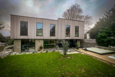 Large and brown modern two floor rear house exterior in Kent with wood cladding, a flat roof, a mixed material roof, a black roof and board and batten cladding.