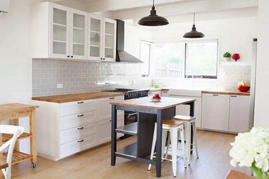 Inspiration for a mid-sized country u-shaped eat-in kitchen in Melbourne with a farmhouse sink, glass-front cabinets, white cabinets, wood benchtops, grey splashback, ceramic splashback, black appliances, laminate floors and with island.