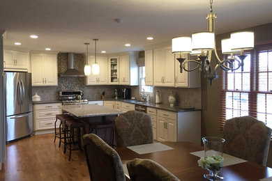 Eat-in kitchen - mid-sized transitional u-shaped eat-in kitchen idea in Omaha with an undermount sink, raised-panel cabinets, white cabinets, gray backsplash, stainless steel appliances and an island