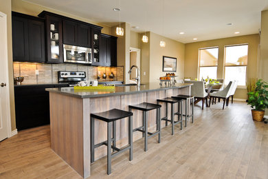 Inspiration for a mid-sized modern galley light wood floor eat-in kitchen remodel in Denver with shaker cabinets, black cabinets, quartz countertops, beige backsplash, stone tile backsplash, stainless steel appliances and an island