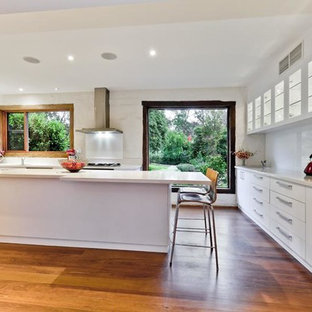 Inspiration pour une très grande arrière-cuisine design en U avec un évier 2 bacs, un placard à porte vitrée, des portes de placard blanches, un plan de travail en terrazzo, une crédence blanche, une crédence en feuille de verre, un électroménager en acier inoxydable, un sol en bois brun, un îlot central et un sol marron.