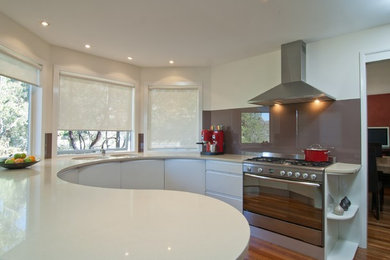This is an example of a mid-sized modern u-shaped kitchen in Canberra - Queanbeyan with an undermount sink, flat-panel cabinets, quartz benchtops, brown splashback, glass sheet splashback, stainless steel appliances and medium hardwood floors.