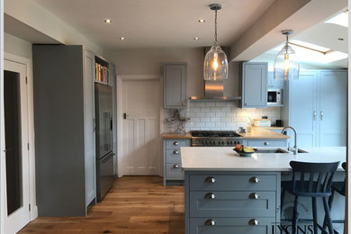 Medium sized contemporary l-shaped open plan kitchen in Other with a submerged sink, shaker cabinets, blue cabinets, marble worktops, stainless steel appliances, medium hardwood flooring, a breakfast bar, brown floors and white worktops.