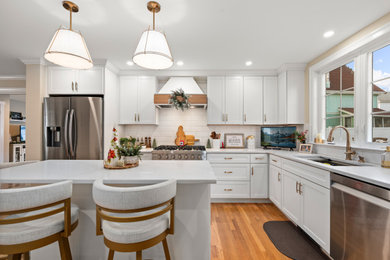 L-shaped medium tone wood floor and brown floor eat-in kitchen photo in Boston with shaker cabinets, white cabinets, white backsplash, subway tile backsplash, stainless steel appliances, an island and white countertops