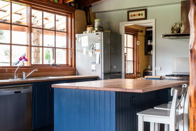 This is an example of a country galley kitchen in Hobart with a drop-in sink, blue cabinets, wood benchtops, stainless steel appliances, dark hardwood floors, with island, brown floor and brown benchtop.