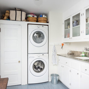 Inspiration for a large nautical l-shaped utility room in Detroit with a submerged sink, glass-front cabinets, white cabinets, stainless steel worktops, white walls, painted wood flooring and a stacked washer and dryer.