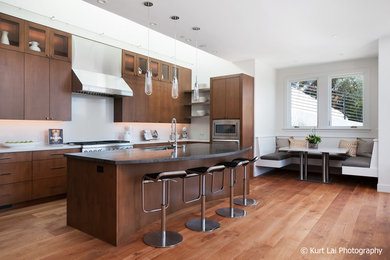 This is an example of a large modern l-shaped open plan kitchen in San Francisco with medium hardwood floors, an undermount sink, flat-panel cabinets, medium wood cabinets, limestone benchtops, white splashback, stone slab splashback, stainless steel appliances and with island.