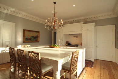 Mid-sized elegant single-wall medium tone wood floor and brown floor open concept kitchen photo in Other with a farmhouse sink, beaded inset cabinets, white cabinets, marble countertops, multicolored backsplash, marble backsplash, paneled appliances and an island