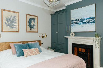 Design ideas for a mid-sized traditional master bedroom in London with white walls, medium hardwood floors, a standard fireplace and brown floor.