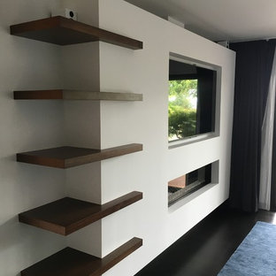Exemple d'une chambre parentale moderne de taille moyenne avec un mur blanc, un sol en bois foncé, une cheminée ribbon, un manteau de cheminée en plâtre et un sol noir.