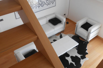 Esempio di un soggiorno design aperto con pareti bianche, parquet chiaro e TV a parete