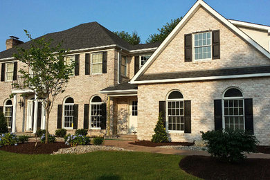 Large traditional beige two-story brick exterior home idea in Philadelphia with a clipped gable roof