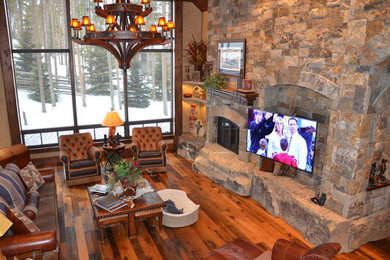 Example of a large mountain style enclosed and formal dark wood floor and brown floor living room design in Denver with beige walls, a standard fireplace, a stone fireplace and a wall-mounted tv