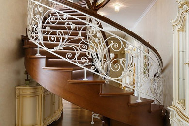 Стильный дизайн: изогнутая деревянная лестница в классическом стиле с деревянными ступенями и металлическими перилами - последний тренд