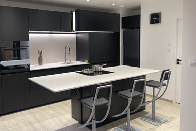 Photo of a large modern galley open plan kitchen in Clermont-Ferrand with an island, an integrated sink, black cabinets, composite countertops, white splashback, engineered quartz splashback, black appliances, ceramic flooring, beige floors, white worktops and a coffered ceiling.