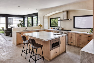 Example of a mid-sized trendy u-shaped concrete floor and gray floor open concept kitchen design in Los Angeles with an undermount sink, flat-panel cabinets, light wood cabinets, quartzite countertops, beige backsplash, ceramic backsplash, stainless steel appliances, an island and beige countertops