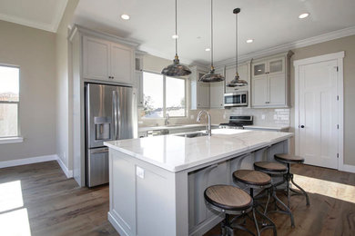 Small modern l-shaped eat-in kitchen in Sacramento with a drop-in sink, beaded inset cabinets, grey cabinets, marble benchtops, white splashback, ceramic splashback, stainless steel appliances, medium hardwood floors, with island, brown floor and white benchtop.