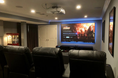 Example of a large classic enclosed carpeted and black floor home theater design in New York with gray walls and a projector screen