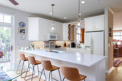 Inspiration for a contemporary l-shaped medium tone wood floor and brown floor eat-in kitchen remodel in Milwaukee with a double-bowl sink, shaker cabinets, white cabinets, quartz countertops, white backsplash, subway tile backsplash, white appliances, a peninsula and white countertops