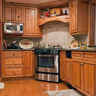 Aménagement d'une arrière-cuisine montagne en L de taille moyenne avec un évier encastré, un placard avec porte à panneau surélevé, des portes de placard en bois brun, un plan de travail en granite, une crédence beige, une crédence en carreau de porcelaine, un électroménager en acier inoxydable, un sol en bois brun et un îlot central.