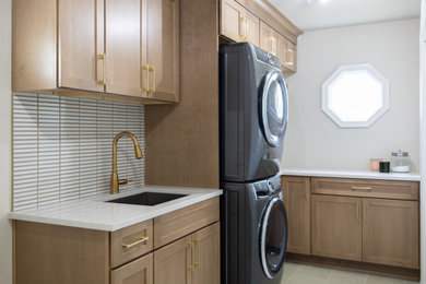 Mid-sized transitional l-shaped beige floor dedicated laundry room photo in Chicago with a drop-in sink, flat-panel cabinets, medium tone wood cabinets, quartz countertops, white backsplash, ceramic backsplash, a stacked washer/dryer and beige countertops