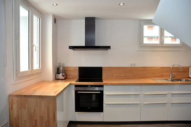 Mid-sized contemporary u-shaped eat-in kitchen in Grenoble with an undermount sink, white cabinets, wood benchtops, brown splashback, timber splashback, black appliances, linoleum floors, grey floor and brown benchtop.