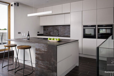 Photo of a small modern single-wall open plan kitchen in Dublin with a single-bowl sink, flat-panel cabinets, grey cabinets, engineered stone countertops, multi-coloured splashback, engineered quartz splashback, black appliances, ceramic flooring, an island, brown floors and multicoloured worktops.