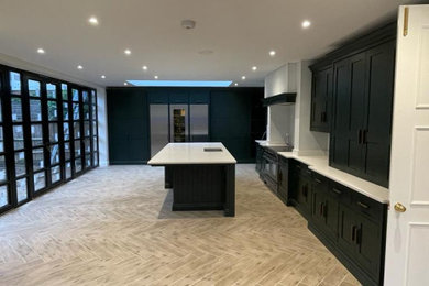 This is an example of an expansive victorian cream and black single-wall open plan kitchen in Buckinghamshire with black appliances, an island and beige worktops.