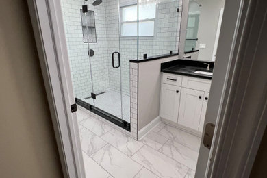 Example of a mid-sized minimalist master white tile and subway tile white floor and single-sink bathroom design in Other with shaker cabinets, white cabinets, a two-piece toilet, gray walls, an undermount sink, quartz countertops, a hinged shower door and black countertops