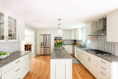 Example of a large transitional u-shaped light wood floor and brown floor eat-in kitchen design in Boston with an undermount sink, shaker cabinets, white cabinets, quartz countertops, gray backsplash, ceramic backsplash, stainless steel appliances, an island and gray countertops