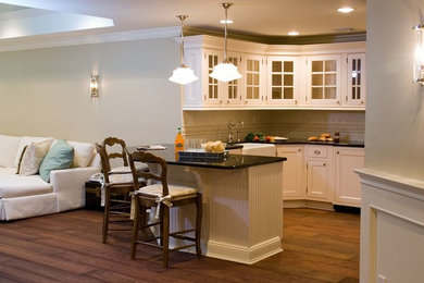 Inspiration for a mid-sized timeless u-shaped dark wood floor and brown floor kitchen remodel in New York with a farmhouse sink, recessed-panel cabinets, white cabinets, beige backsplash, stone tile backsplash, a peninsula and black countertops