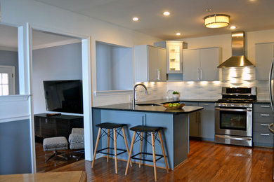 Mid-sized trendy u-shaped medium tone wood floor and brown floor eat-in kitchen photo in Philadelphia with an undermount sink, flat-panel cabinets, gray cabinets, soapstone countertops, white backsplash, porcelain backsplash, stainless steel appliances and a peninsula