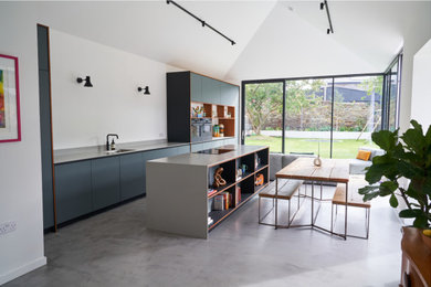Retro single-wall open plan kitchen in Edinburgh with a single-bowl sink, flat-panel cabinets, green cabinets, composite countertops, white splashback, black appliances, an island, grey floors, grey worktops, a vaulted ceiling and feature lighting.